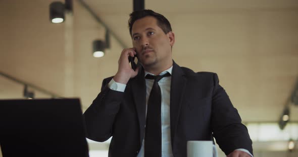 A man in a formal suit talking on the phone, while working at the office. Medium shot, slow motion