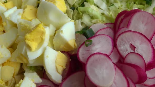 Salad ingredients in a glass bowl, cabbage, radish, onion, cucumber, egg.