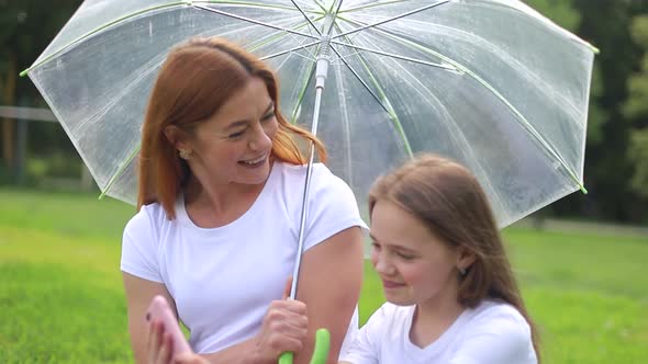 Happy mother smiles and plays with her daughter in the park hiding from the rain.