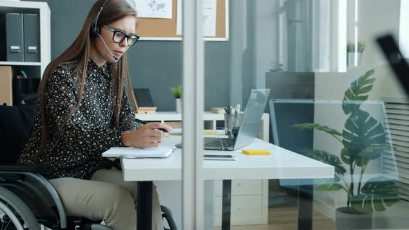 Cheerful Handicapped Girl Employee Talking to Clients Online with Laptop and Headphones Laughing