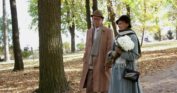 Elderly Lovely Married Couple with Bouquet of Flowers Walking in Park with Joy