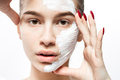 Young woman with a white cosmetic mask on a half of her face holds her hands at her face on the - PhotoDune Item for Sale