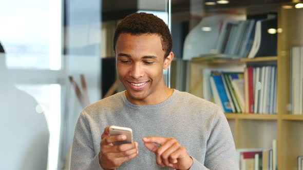 Young African Man Browsing Online on Smartphone