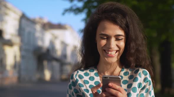 Portrait of Caucasian Cheerful Woman Wearing Dress Smiling While Holding and Using Smartphone During