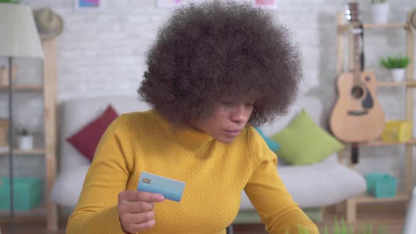 Beautiful African American Girl with an Afro Hairstyle with a Bank Card in Hand and a Laptop in the