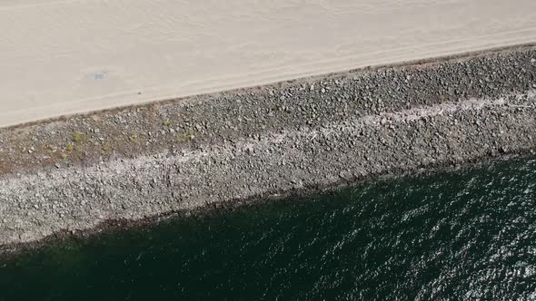 Turn over the shore of a lbig lake with the camera facing down. During the turn, the camera turns up