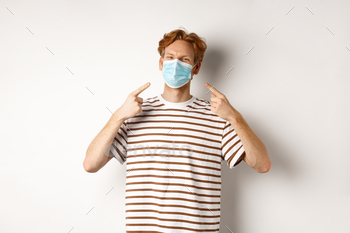 Covid, virus and social distancing concept. Smiling redhead guy pointing fingers at face mask / Photodune, Misc