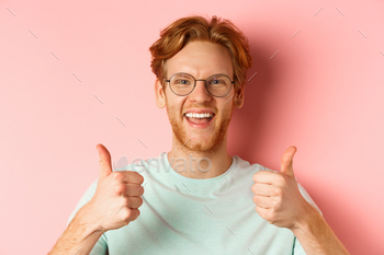 Face of satisfied male customer showing thumbs-up in approval, smiling happy, wearing glasses and t / Photodune, Misc