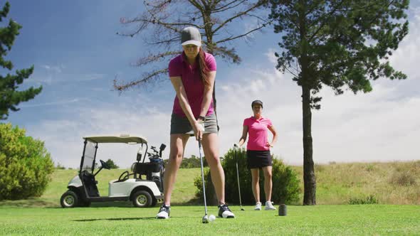 Two caucasian women playing golf one taking shot from bunker