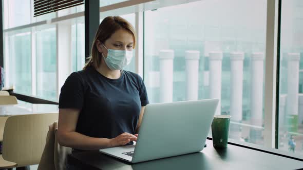 Young Woman Wearing Protective Face Mask While Working Remotely on Laptop in Coffee Shop