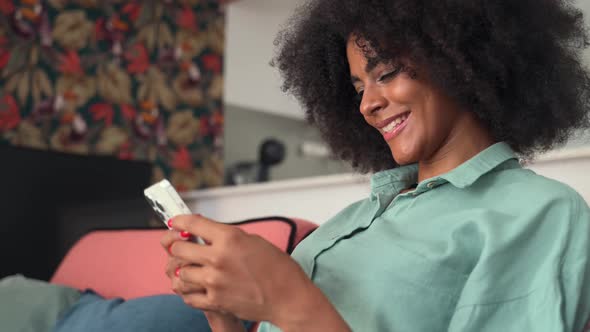Charming Multiethnic Woman with Afro Hairstyle Using Smartphone at Home