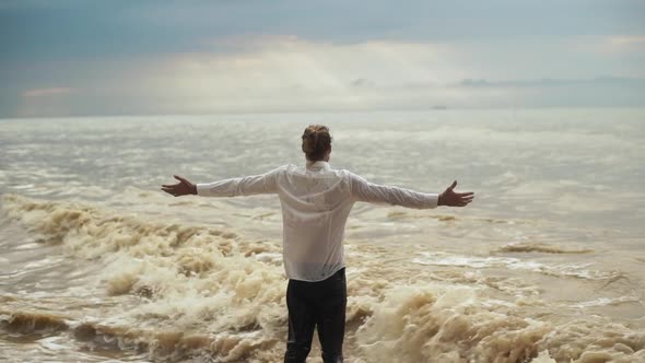 Man with Tied Hair in Clothes Standing Into Sea and Greeting Force of Nature with Open Arms Feeling