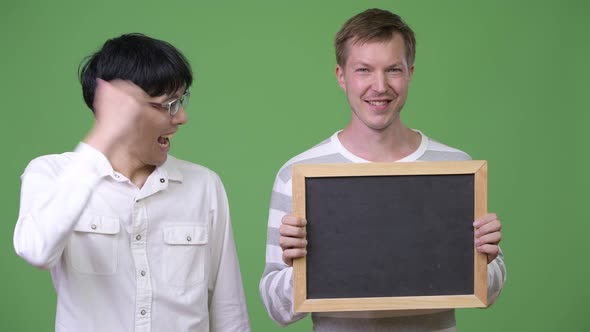 Two Happy Young Multi-ethnic Businessmen Showing Blackboard and Giving Thumbs Up