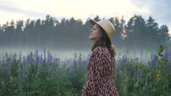 Happy Romantic Girl in a Dress and Hat Walks Along the Field with Flowers and Fog, Dances Inspired