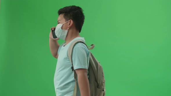 Asian Boy Student Wearing A Mask And Talking On Mobile Phone While Walking On Green Screen