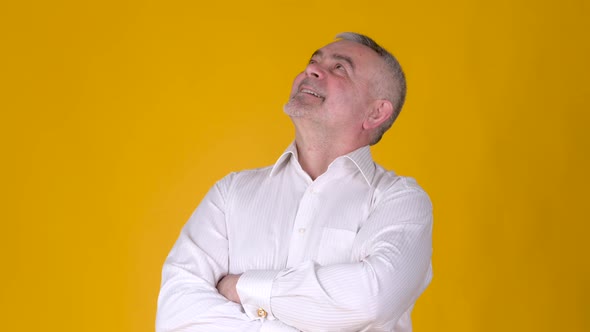 Caucasian male with folded arms looking up on yellow studio background.