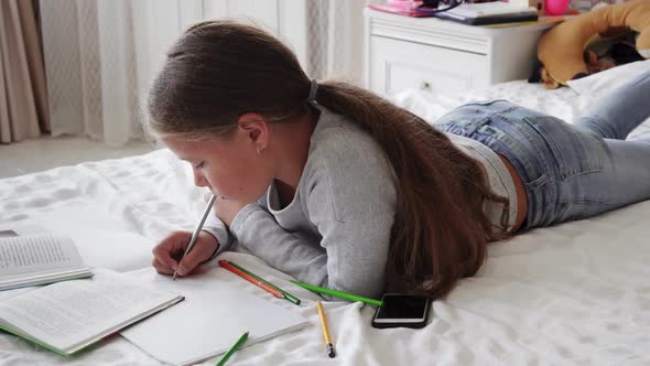 Little School Girl Lying on Bed and Doing Homework