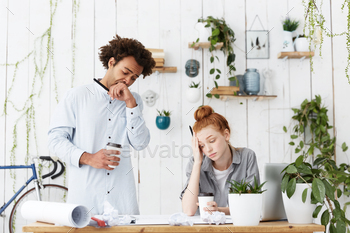 Candid shot of two tired and sleepy young man and woman architects facing deadline working together