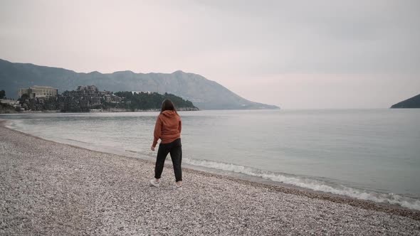 Lonely Young woman walks along the sea in spring cloudy weather