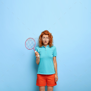 s with indignant expression, surprised to loose match, wears casual clothing, isolated on blue wall, blank space above. Athletic woman has training