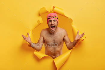 le paper, shouts with negative emotions, wears swimhat and goggles, has naked body, yellow background. Place for information. Negative emotions