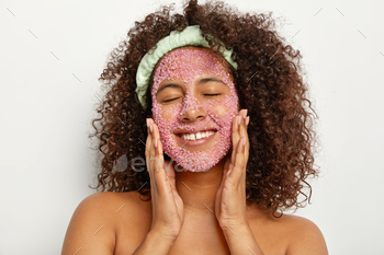 ith sea salt, smiles happily, keeps eyes shut gets facial treatment for smooth soft skin reduces dark dots wears headband on head, has well cared body