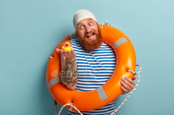 ll toy duckling, has fun on shore, enjoys safe swimming with lifebuoy and swimhat, spends summer holidays, isolated on blue background. Recreation