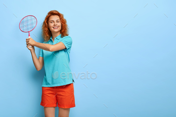 casual blue t shirt and red shorts, enjoys game with friend, has happy expression, stands against blue studio wall with copy space for your promotion