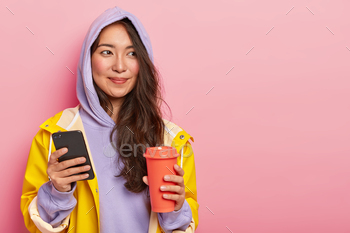 ses modern cellphone for chatting with friends, holds takeaway coffee, isolated over pink background. People, technolgy and lifestyle concept