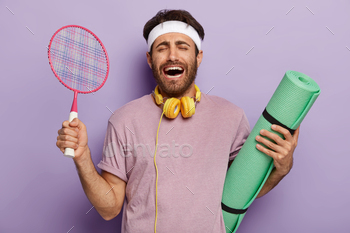 ennis racket, laughs with overjoyed expression, has dark hair, dressed in casual wear, listens music during training, isolated over purple background.