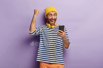 tes winning lottery, gets message of confirming holds mobile phone, browses social media, wears yellow hat, striped jumper, always stays in touch