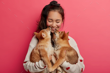 ut words. Cheerful korean woman receives kiss from two pedigree puppies, cannot imagine life without pets, has fun with animal best friends.