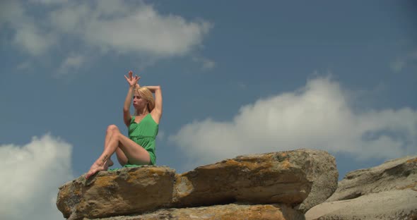 Woman in Green Dress is Sitting on Top of a Cliff and Moving Her Hands Around