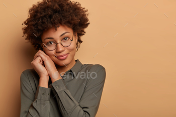 n woman entrpreneur has relieved expression after finishing necessary task from boss, tilts head and keeps hands near face, isolated on brown wall
