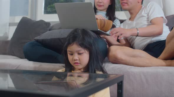 Young Asian family and daughter happy using tablet and laptop at home.