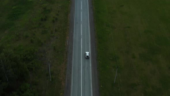 Aerial View of a Car Driving Along the Road Among Fields of Green Grass