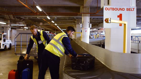 Two airport workers putting baggage on baggage carousel