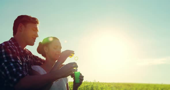 Romantic couple blowing bubbles in mustard field