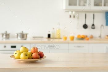  for rent. Plate with apples on table, bottles of sauces and utensils, orange juice in glasses and fruits, light walls and white furniture, copy space