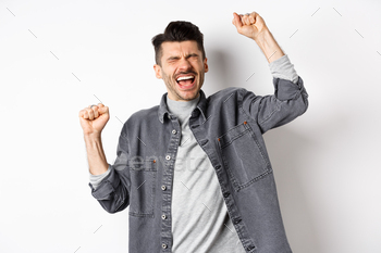 reaming yes, making fist pump with pleased and relieved face, achieve goal and celebrating, triumphing as winning prize, white background.
