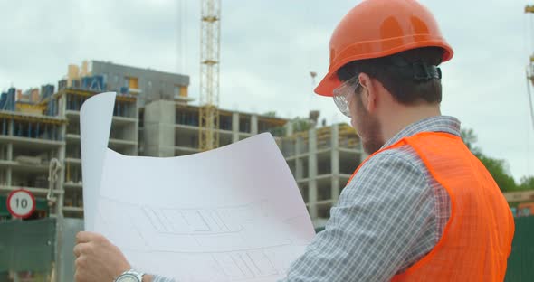 Close-up Portrait of Engineer with Blueprint on Background of Building Under Construction. Young