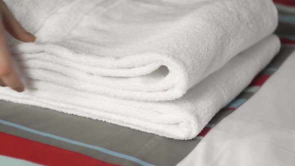 Closeup of Hands Putting Stack of Fresh White Bath Towels on the Bed Sheet