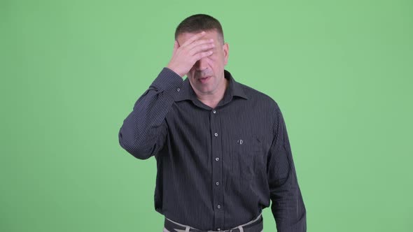 Serious Macho Mature Businessman Pointing and Showing Face Palm Gesture