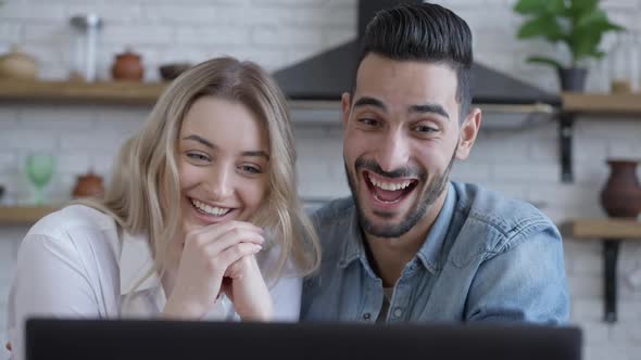 Joyful Caucasian Woman and Middle Eastern Man Watching Comedy Movie Online on Laptop Talking and