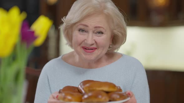 Portrait of Joyful Smiling Senior Woman Bragging Freshlybaked Buns Posing Indoors at Home