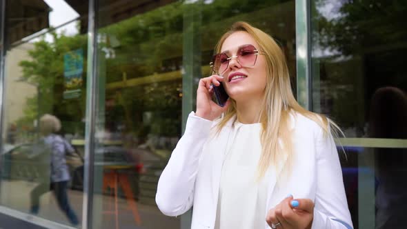 Cheerful Blonde Woman in Fashionable Outfit Talking on Phone on the Street 
