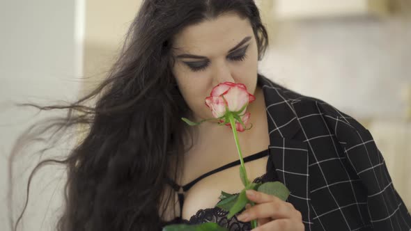 Portrait of Adorable Overweight Woman Sniffing Rose Indoors. The Hair Fluttering on the Wind