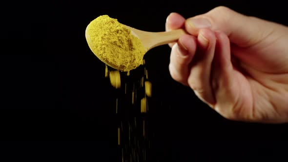 Adding Turmeric Powder to Dish on Black Background Using Seasoning and Flavors