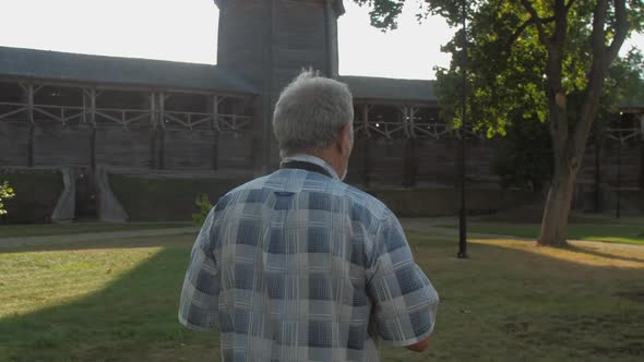 Pensioner Holds Black Camera and Takes Photo in Museum Park