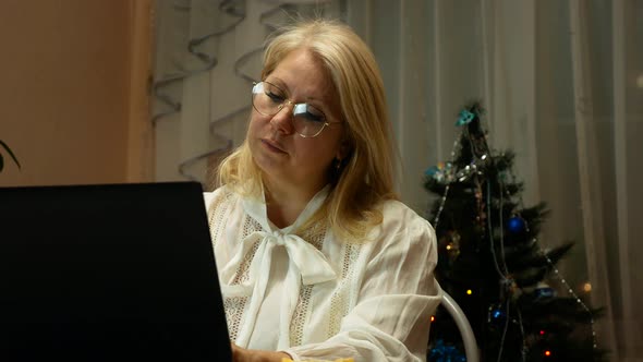 Caucasian blonde woman over 40 works at home on a computer during the holidays